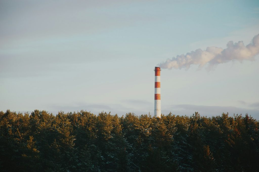 Usine industrielle avec cheminée fumante à proximité d'une zone boisée