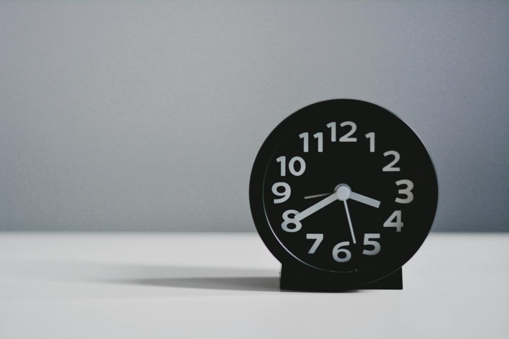 Minimalistischer schwarzer Wecker auf einem Schreibtisch, Symbol für Zeitdruck am Arbeitsplatz