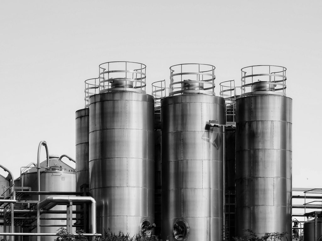 Three tall stainless steel industrial storage tanks with railings under a clear sky