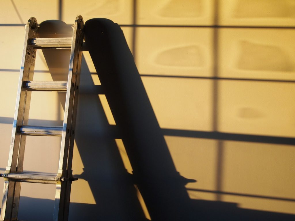 Ladder against a white wall with shadow patterns cast by sunlight