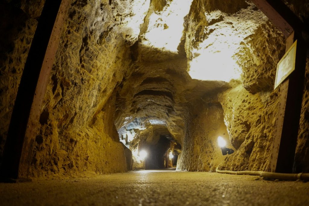 Illuminated underground mine tunnel with rock walls and timber/steel ground support structure